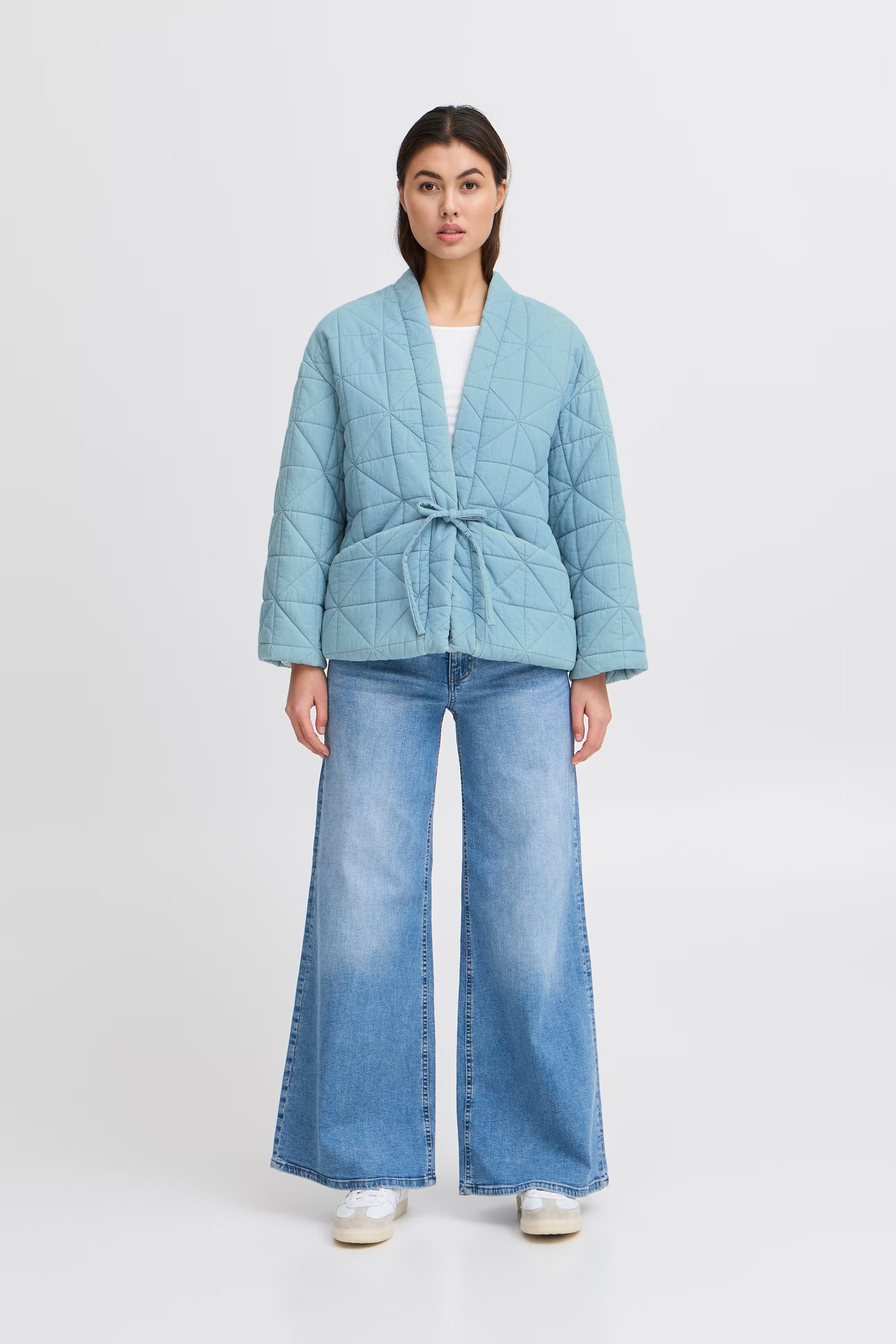 Woman wearing a light blue quilted jacket and jeans on a white background