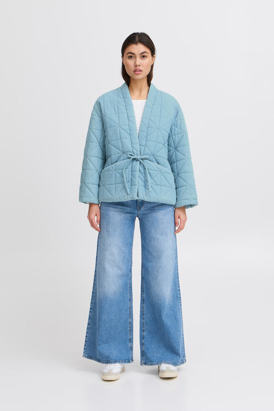 Woman wearing a light blue quilted jacket and jeans on a white background