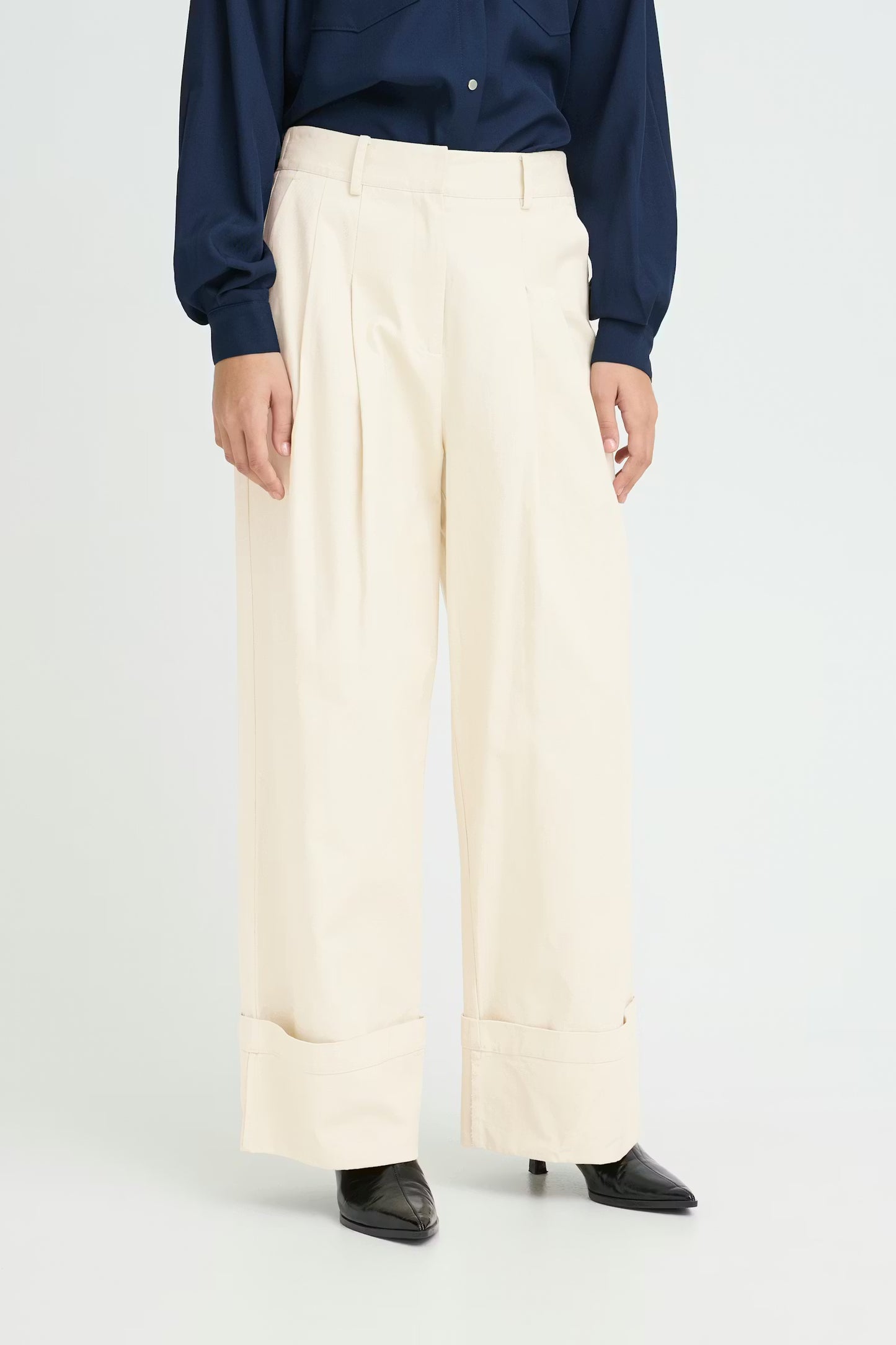 Close up of Women wearing cream trousers with navy shirt. White studio background
