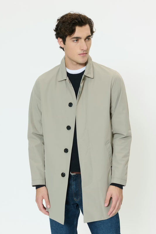Man wearing a light gray coat over a black shirt and blue jeans on a white background