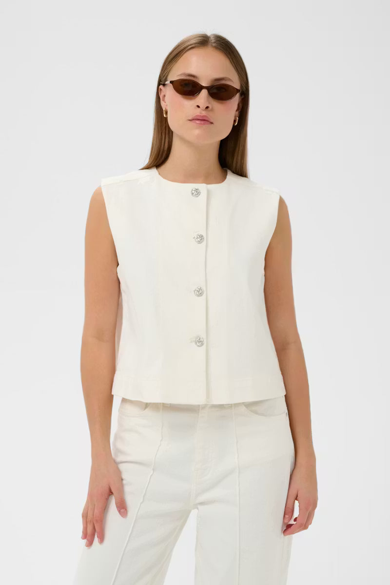 Woman wearing a white sleeveless top and pants with sunglasses on a light gray background