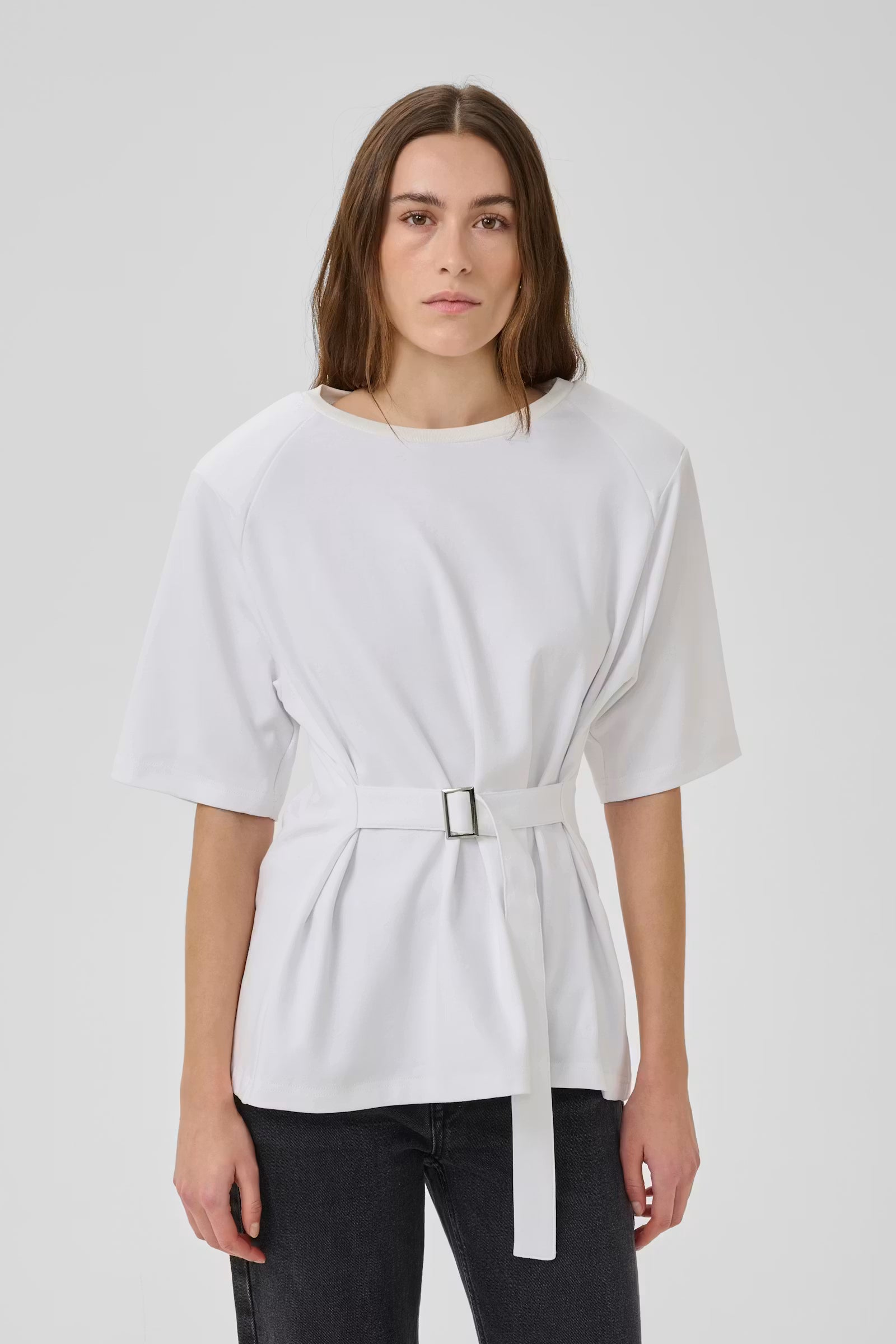 Woman wearing a white top with a belt against a plain background