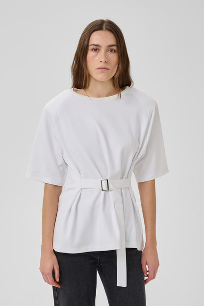 Woman wearing a white top with a belt against a plain background