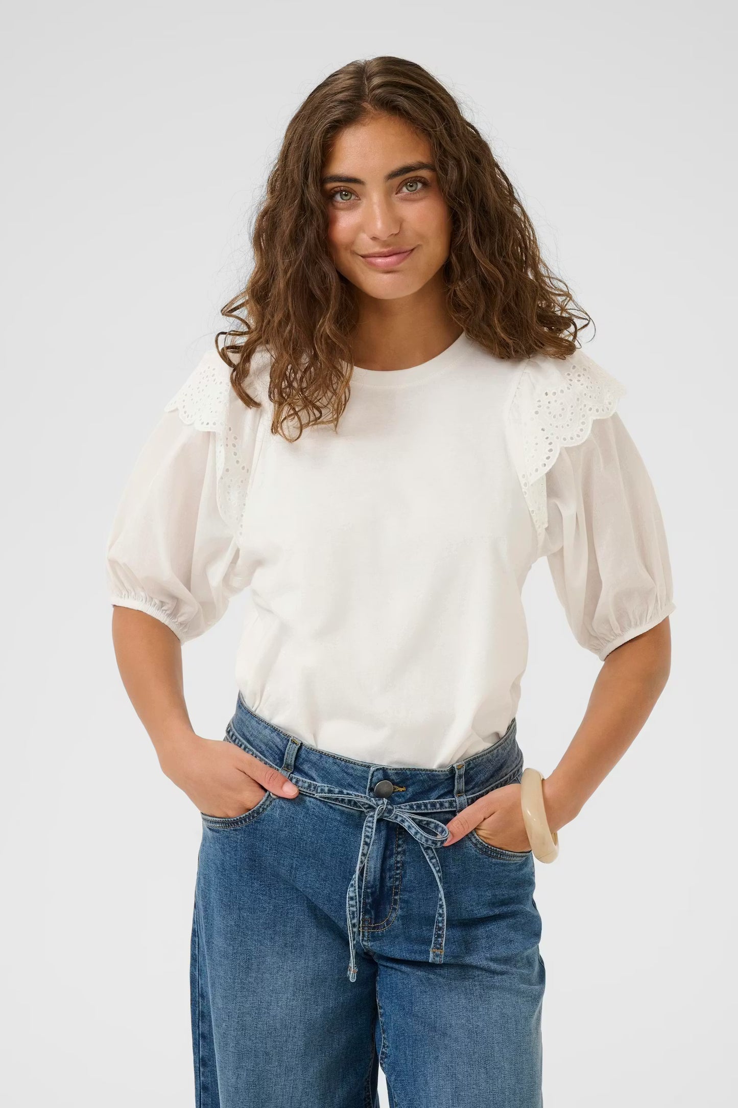 Woman wearing a white blouse with lace details and blue jeans on a plain background