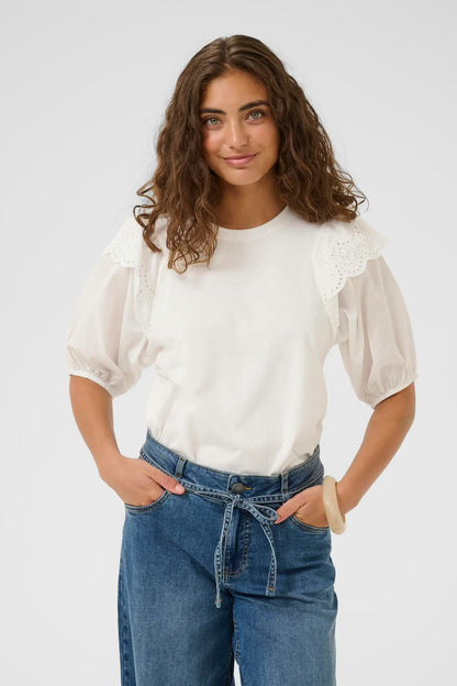 Woman wearing a white blouse with lace details and blue jeans on a plain background