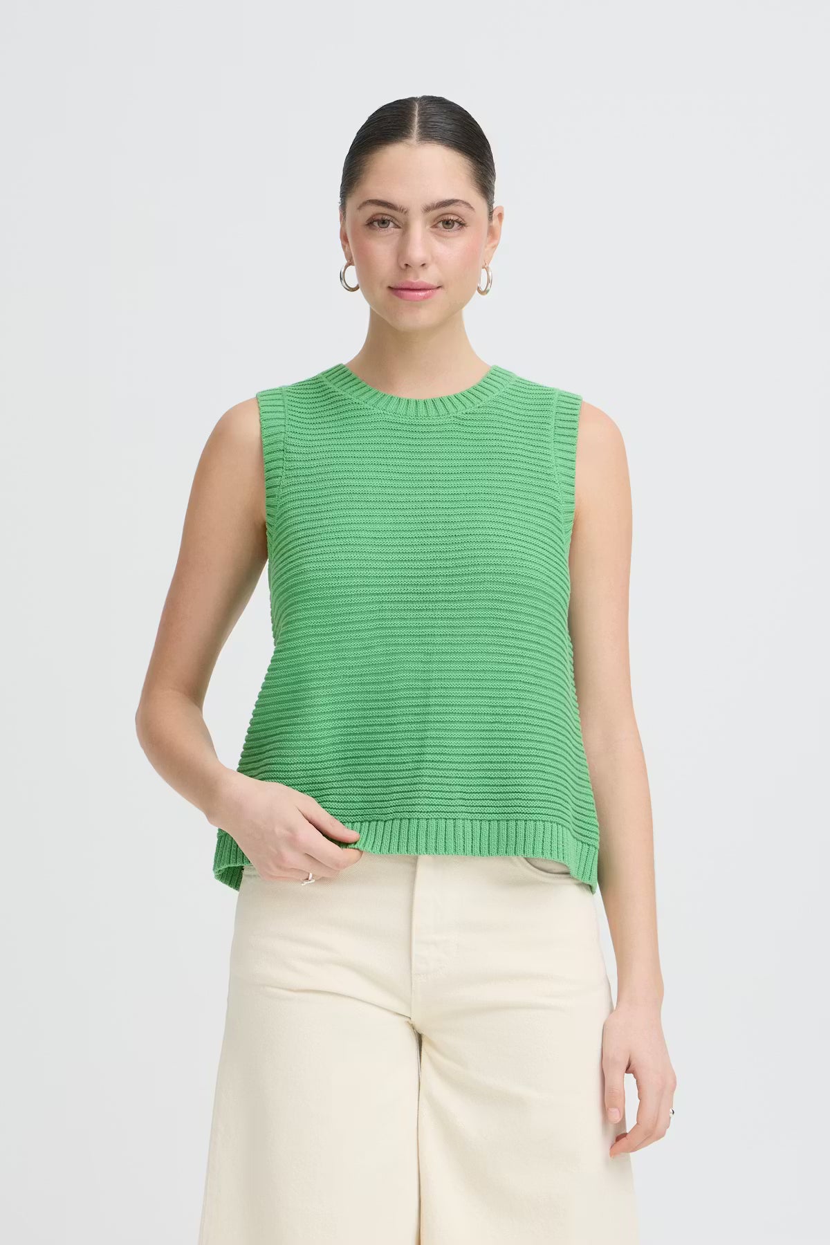 Woman wearing a green sleeveless top and beige pants on a white background