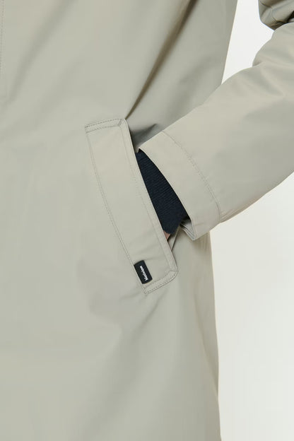 Close-up of a beige coat with a visible brand label on a light gray background