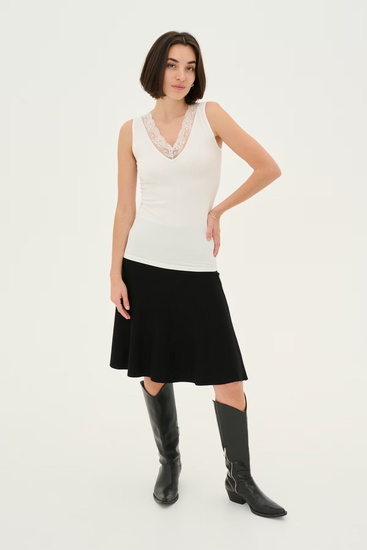 Woman wearing a white sleeveless top with lace detail and a black skirt on a white background