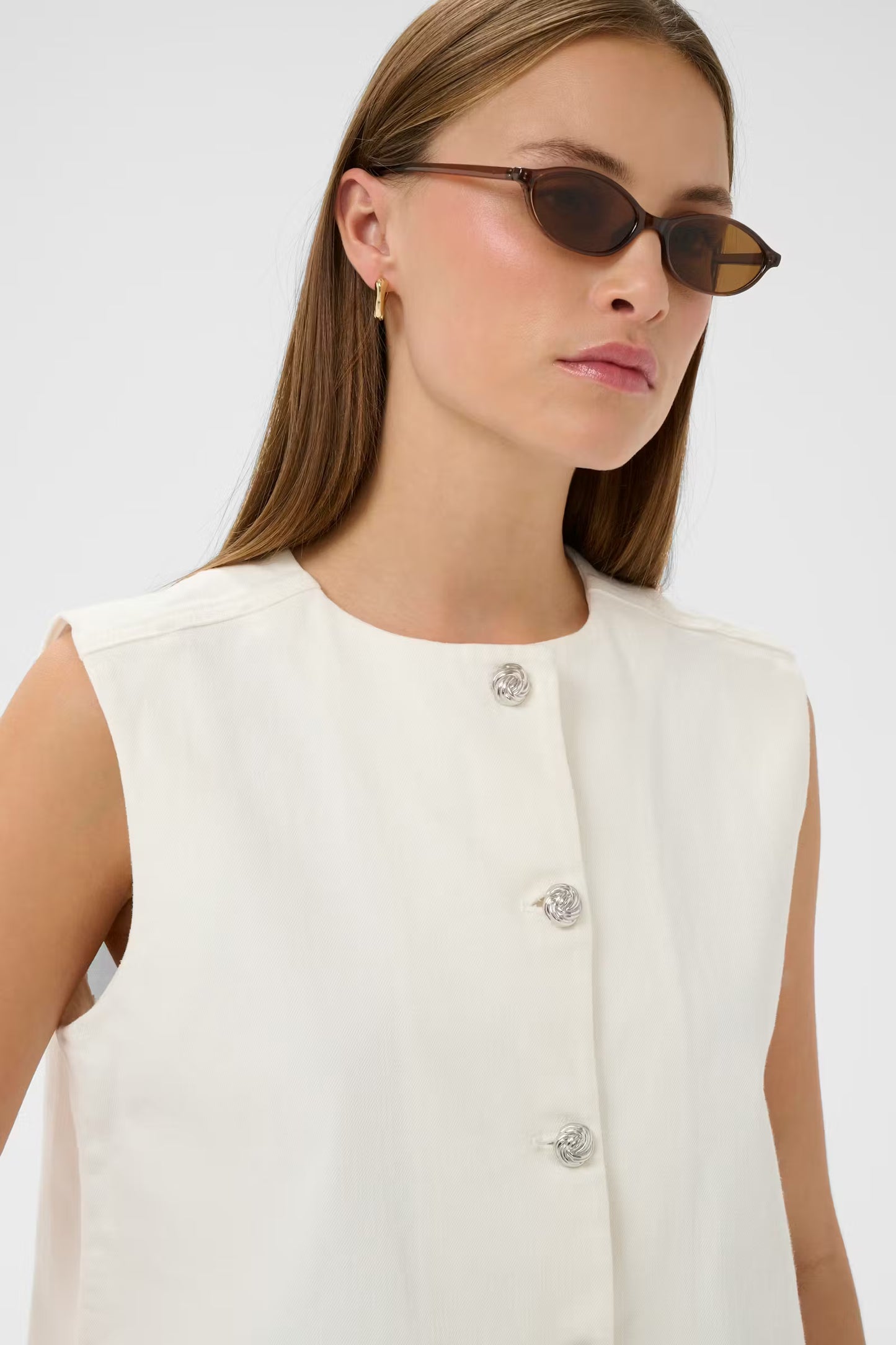 Woman wearing a white sleeveless top with floral buttons against a plain background