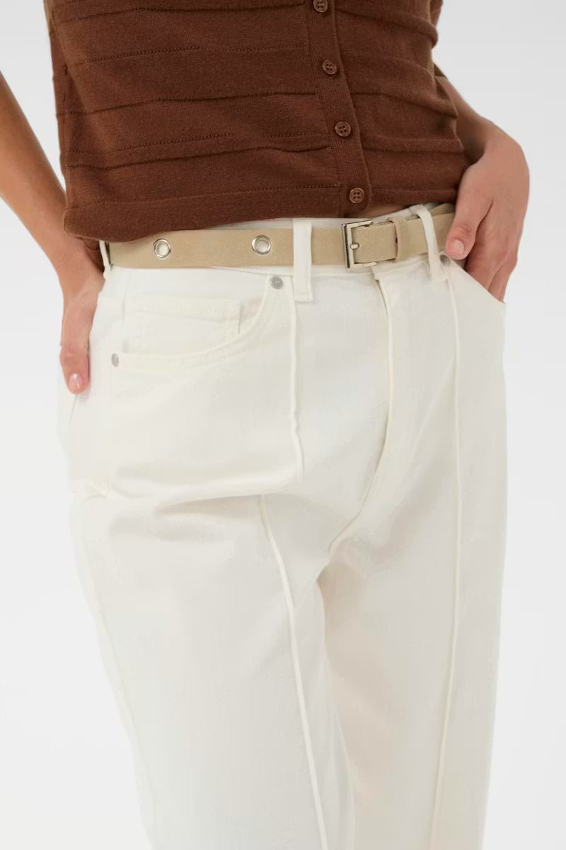 Person wearing a brown top and white pants with a beige belt on a white background