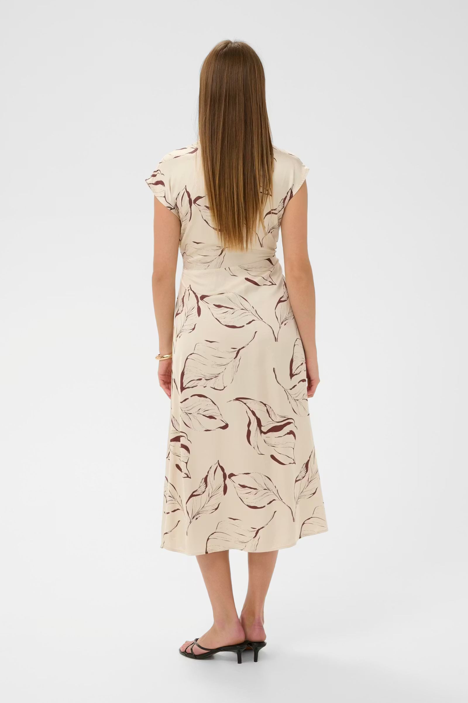 Woman wearing a beige dress with a leaf pattern on a white background