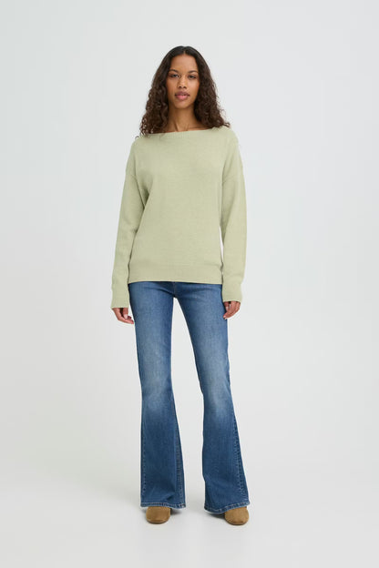 Woman wearing a light green sweater and blue jeans on a white background