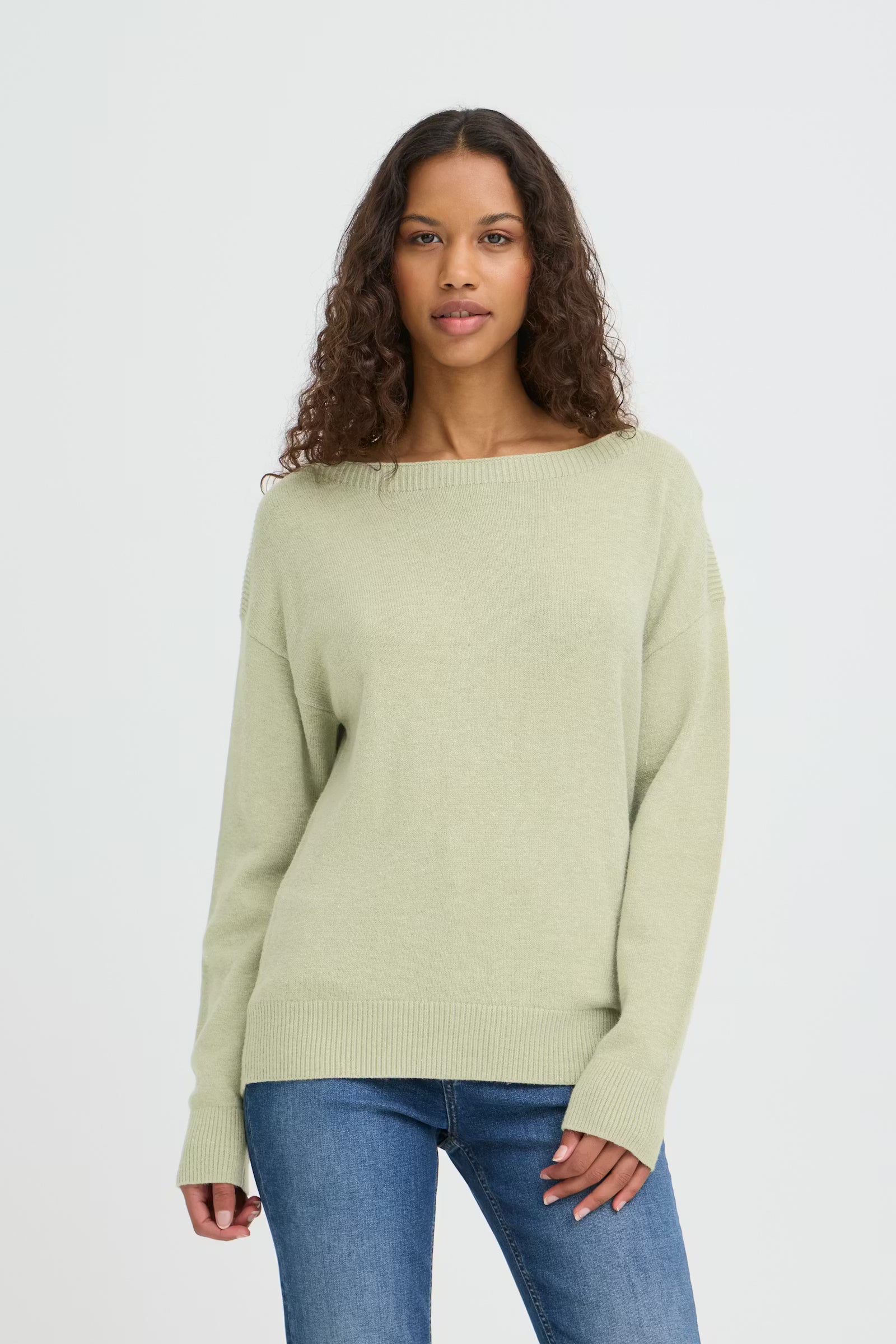 Woman wearing a light green sweater and blue jeans on a white background
