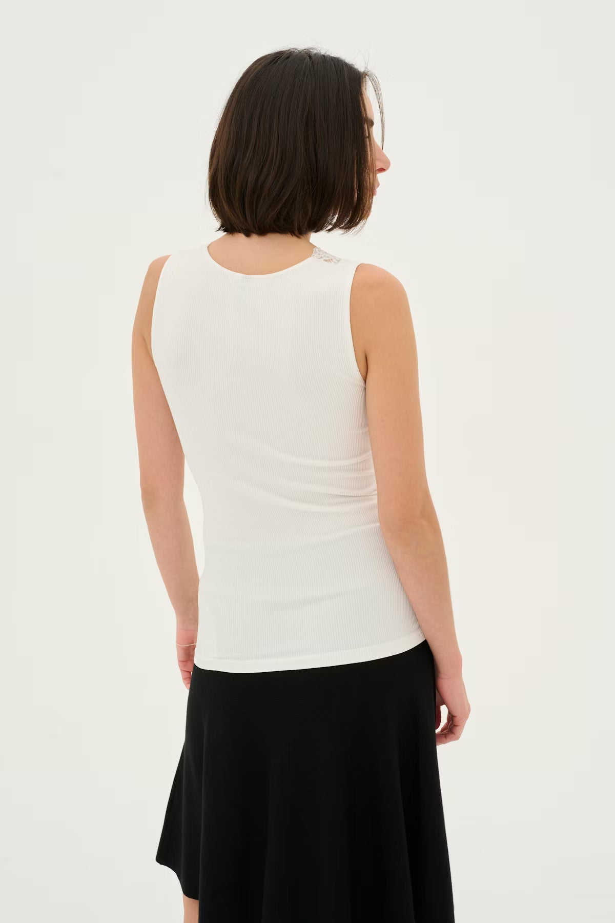 Woman wearing a white sleeveless top with lace detail and a black skirt on a white background