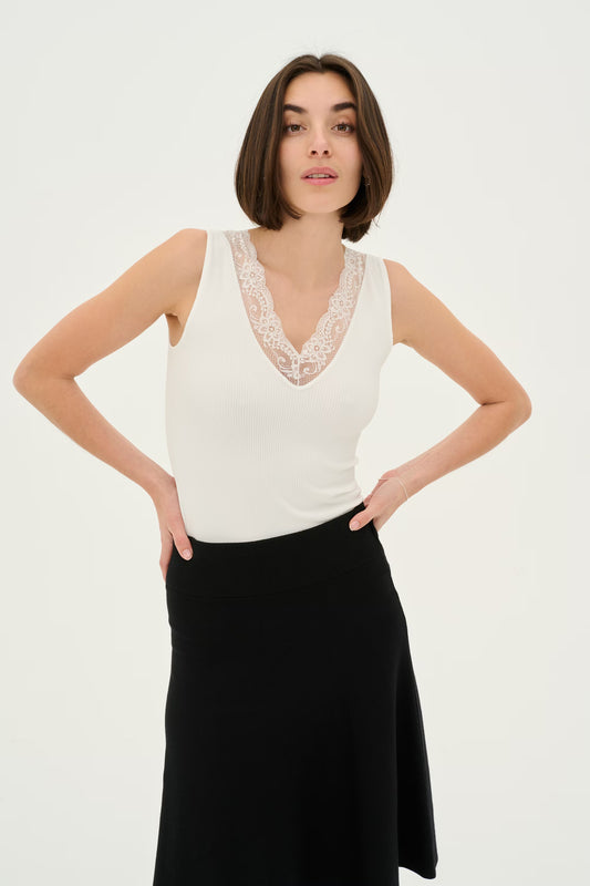 Woman wearing a white sleeveless top with lace detail and a black skirt on a white background