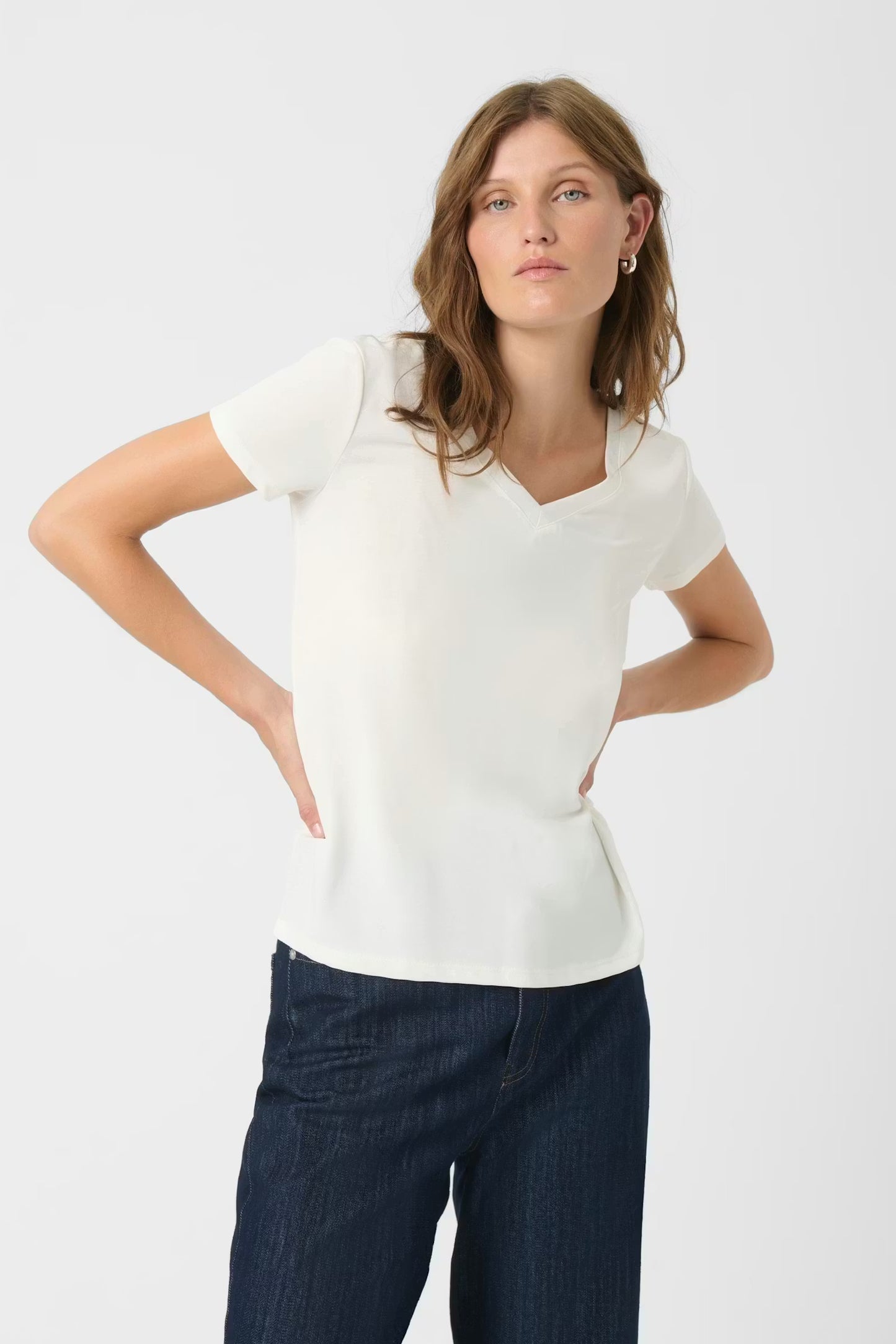 Woman wearing a white t-shirt and dark blue jeans on a light gray background