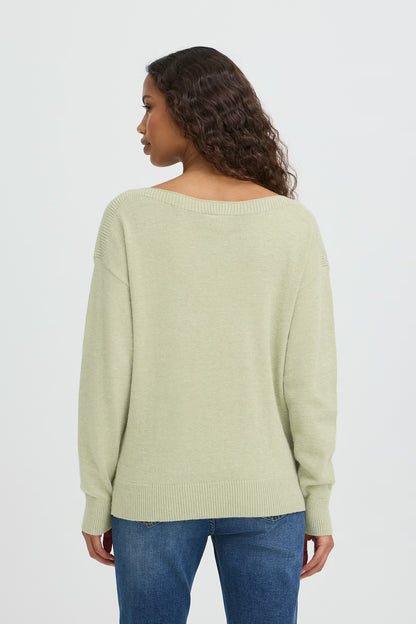 Woman wearing a light green sweater and blue jeans on a white background