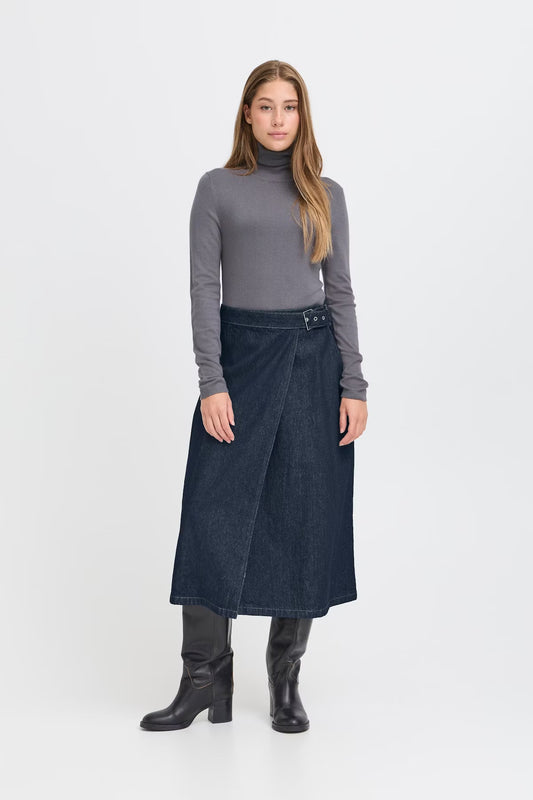 Woman wearing a gray turtleneck, dark denim skirt, and black boots on a white background