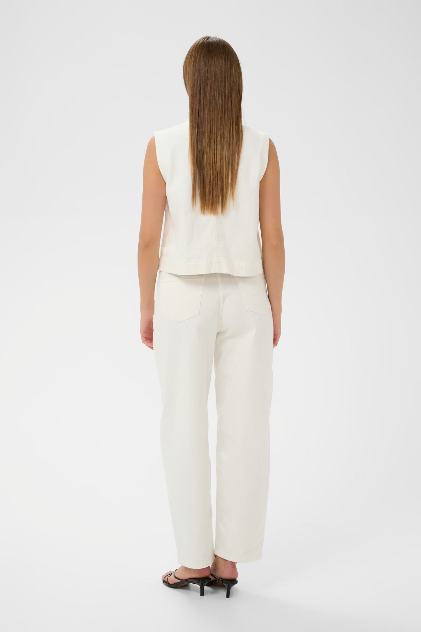 Woman wearing a white sleeveless top and pants on a white background