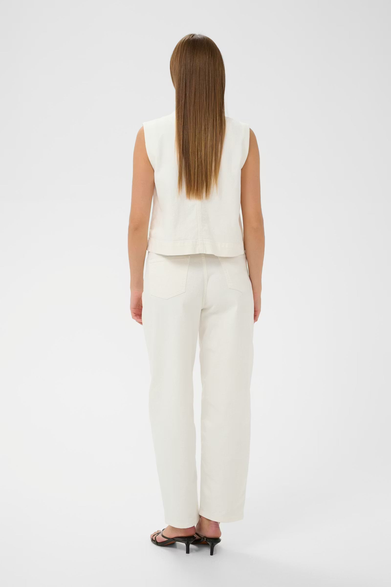 Woman wearing a white sleeveless top and pants on a white background