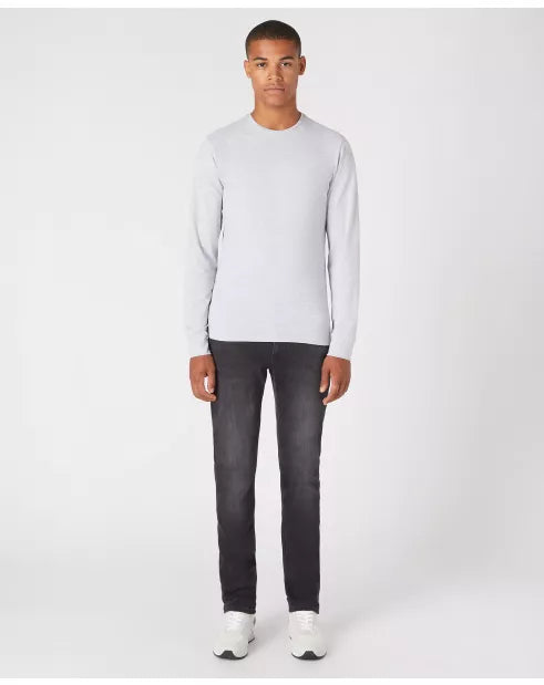 Man wearing a light gray sweater and black jeans on a white background