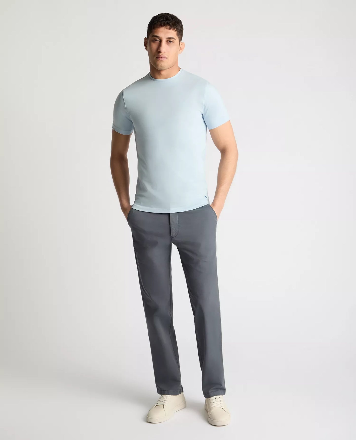 Man wearing a light blue t-shirt and gray pants on a white background