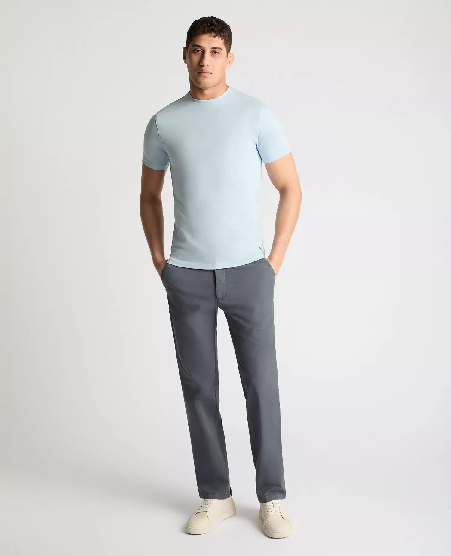 Man wearing a light blue t-shirt and gray pants on a white background