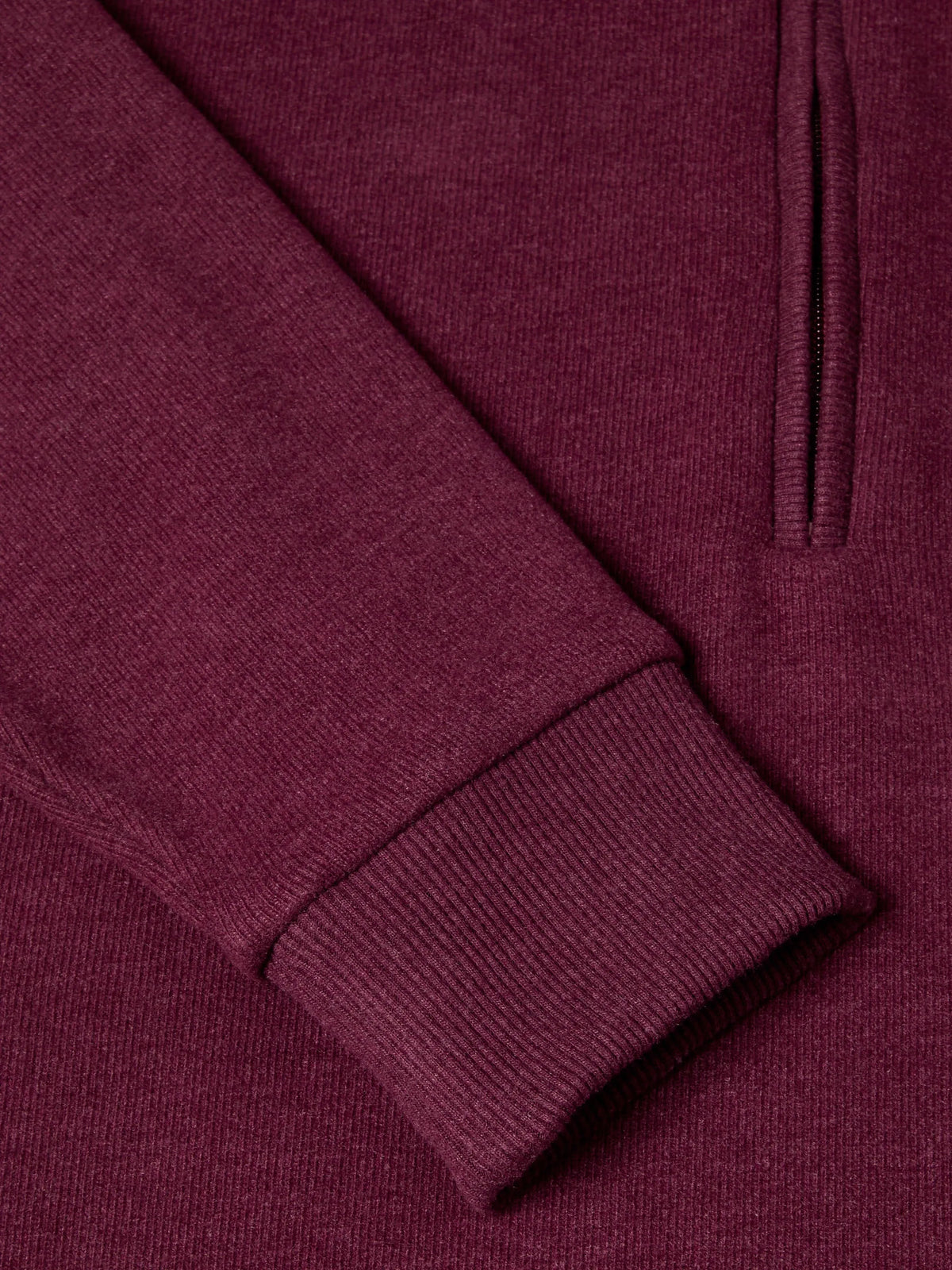 Close-up of a ribbed knit garment in a deep burgundy or plum purple color, showing the texture of the fabric and a portion of a vertical zipper.