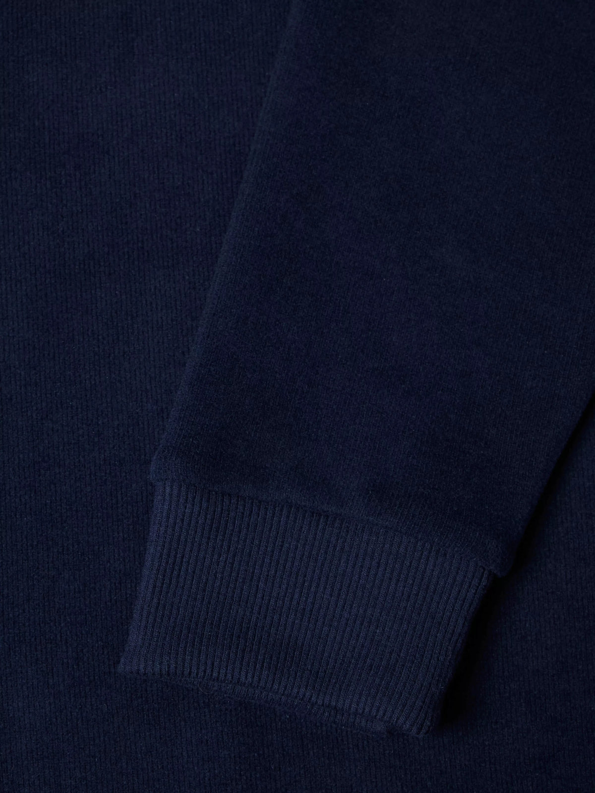 Close-up of a dark navy ribbed knit fabric, showing the texture and cuff detail of a garment.