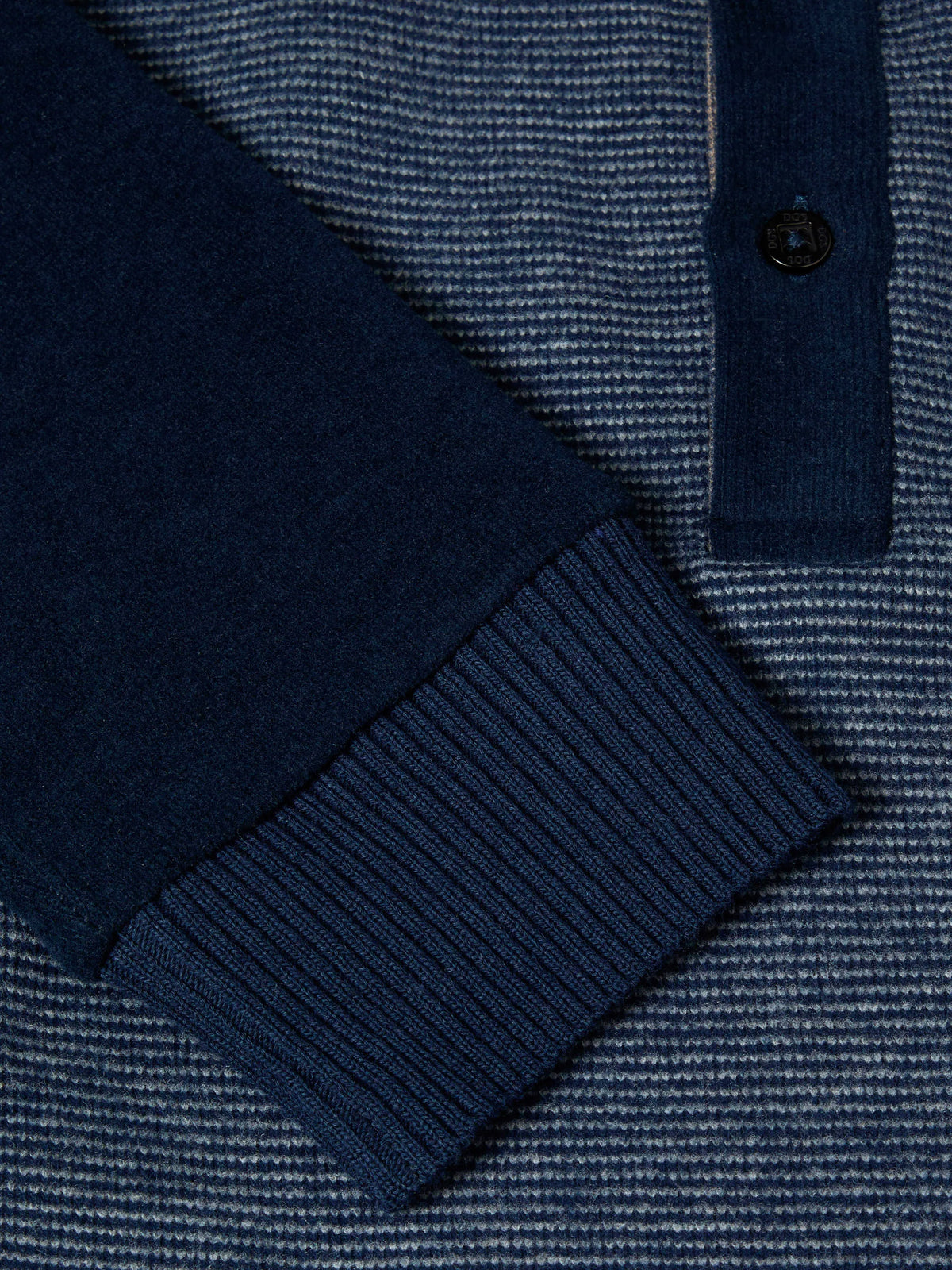 Close-up of a navy blue ribbed knit long-sleeve polo shirt, showing the sleeve cuff, button placket, and textured striped fabric body.
