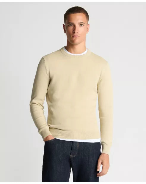 Man wearing a beige sweater and dark jeans on a light gray background