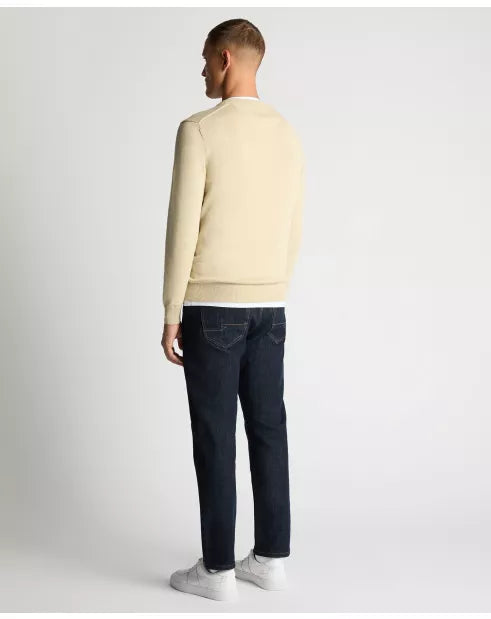 Man wearing a beige sweater and dark jeans on a white background