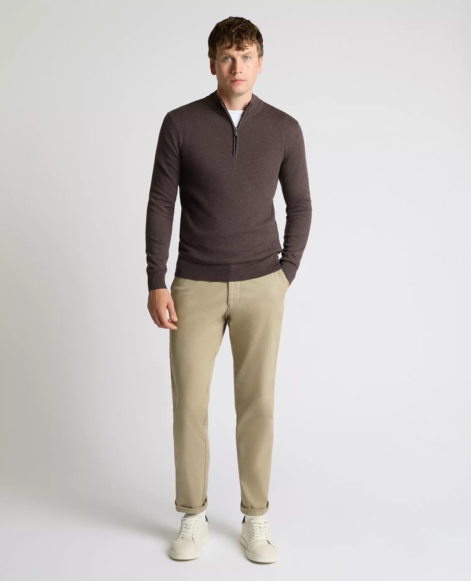 Man wearing a brown long-sleeve shirt and beige pants on a white background