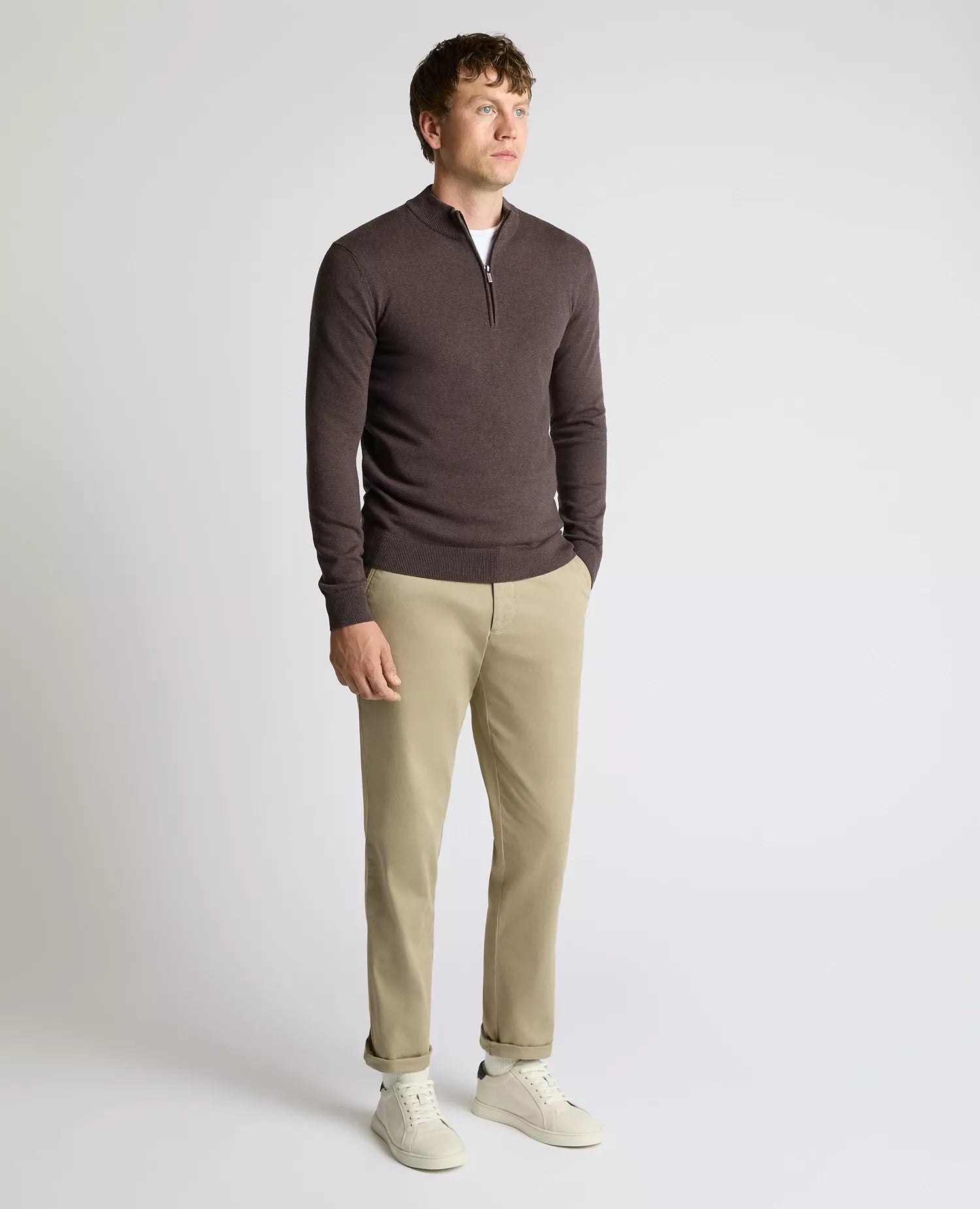 Man wearing a brown sweater and beige pants on a white background