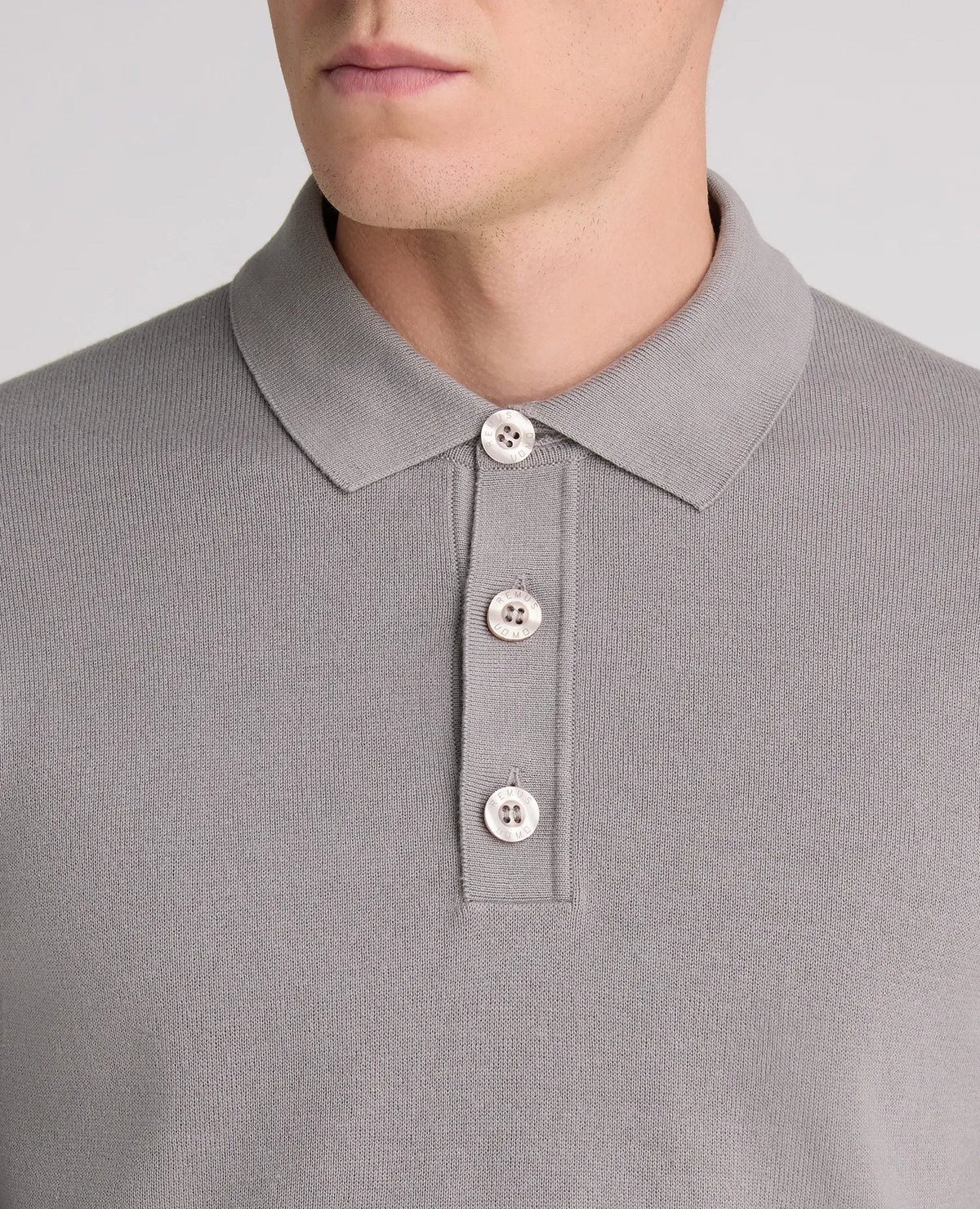 Close-up of a man wearing a light gray ribbed knit polo shirt with a three-button placket.