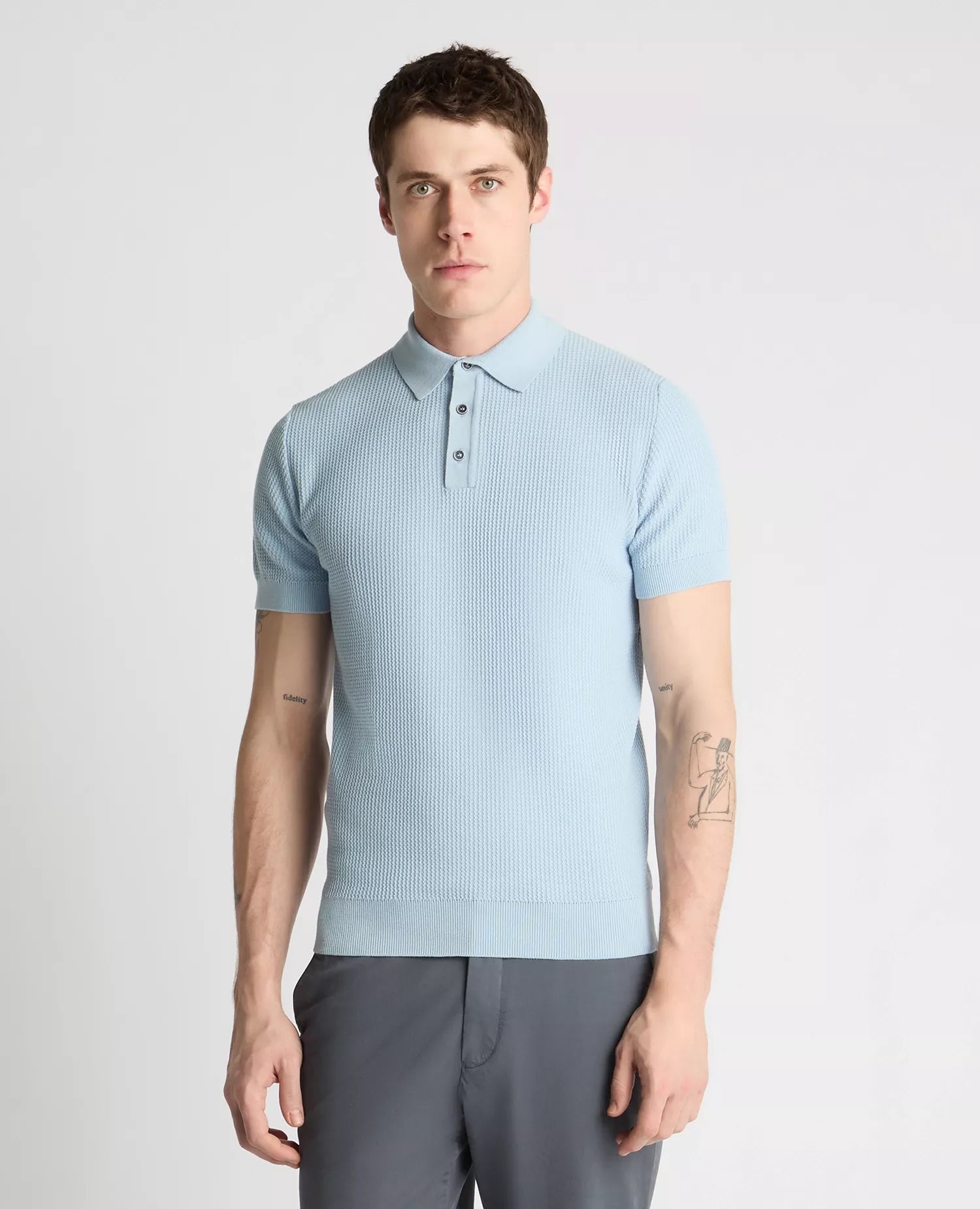 Man wearing a light blue textured polo shirt and gray pants on a white background