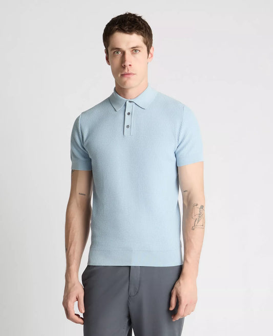 Man wearing a light blue textured polo shirt and gray pants on a white background