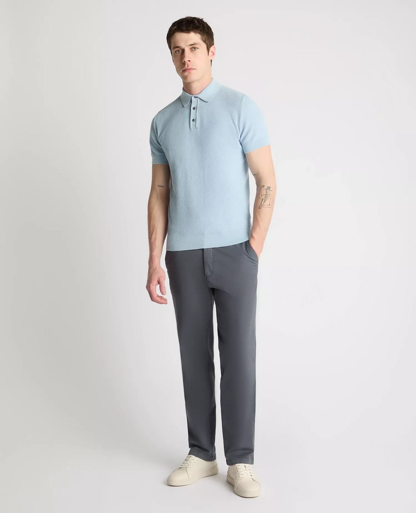 Man wearing a light blue polo shirt and gray pants on a white background