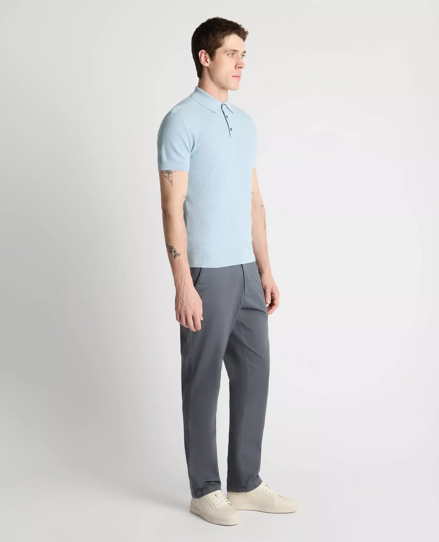 Man wearing a light blue polo shirt and gray pants on a white background