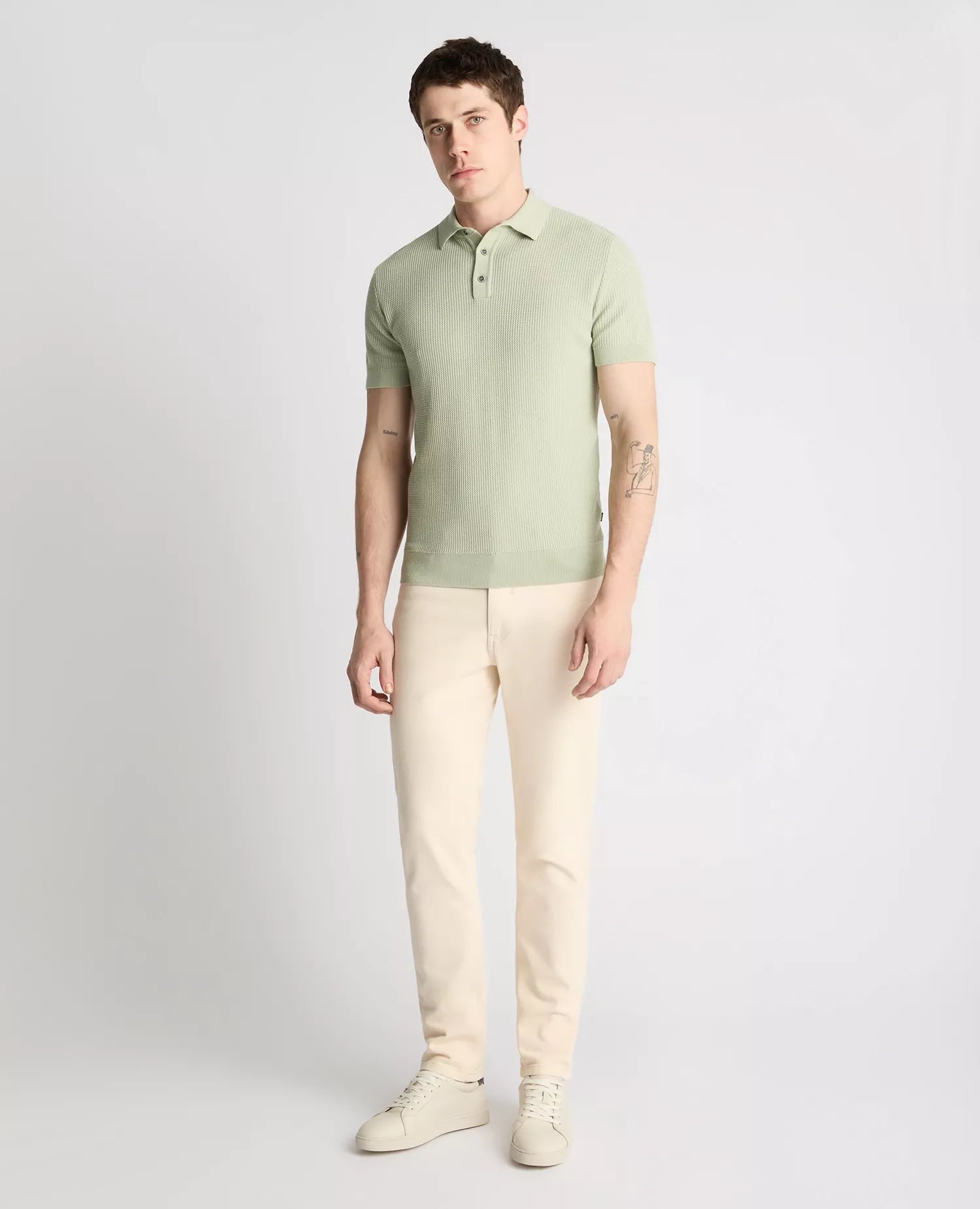 Man wearing a light green polo shirt and beige pants on a gray background