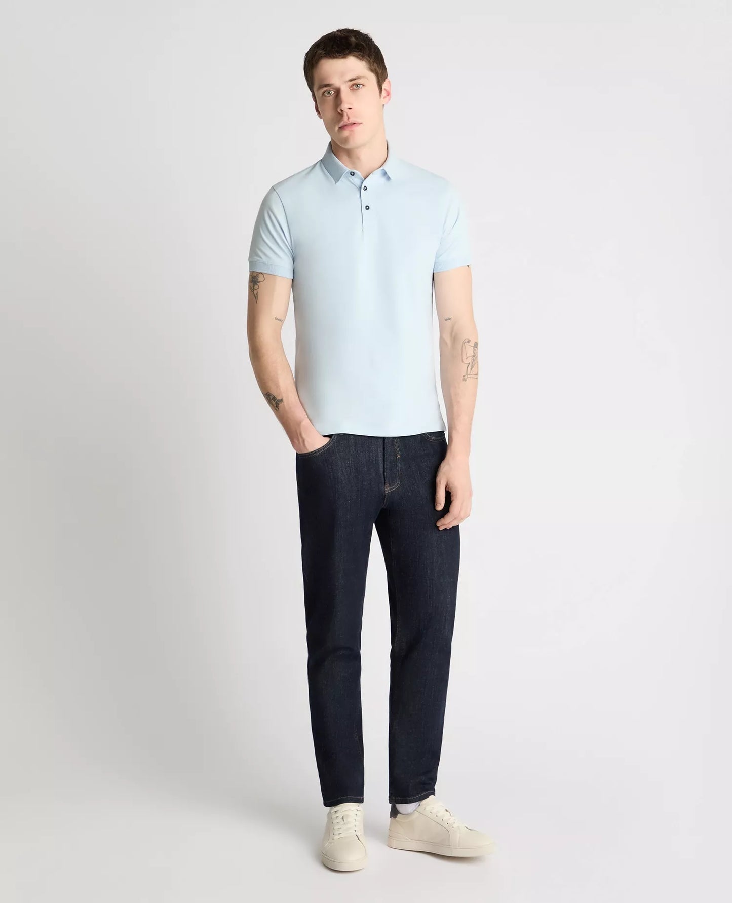Man wearing a light blue polo shirt and dark jeans on a white background