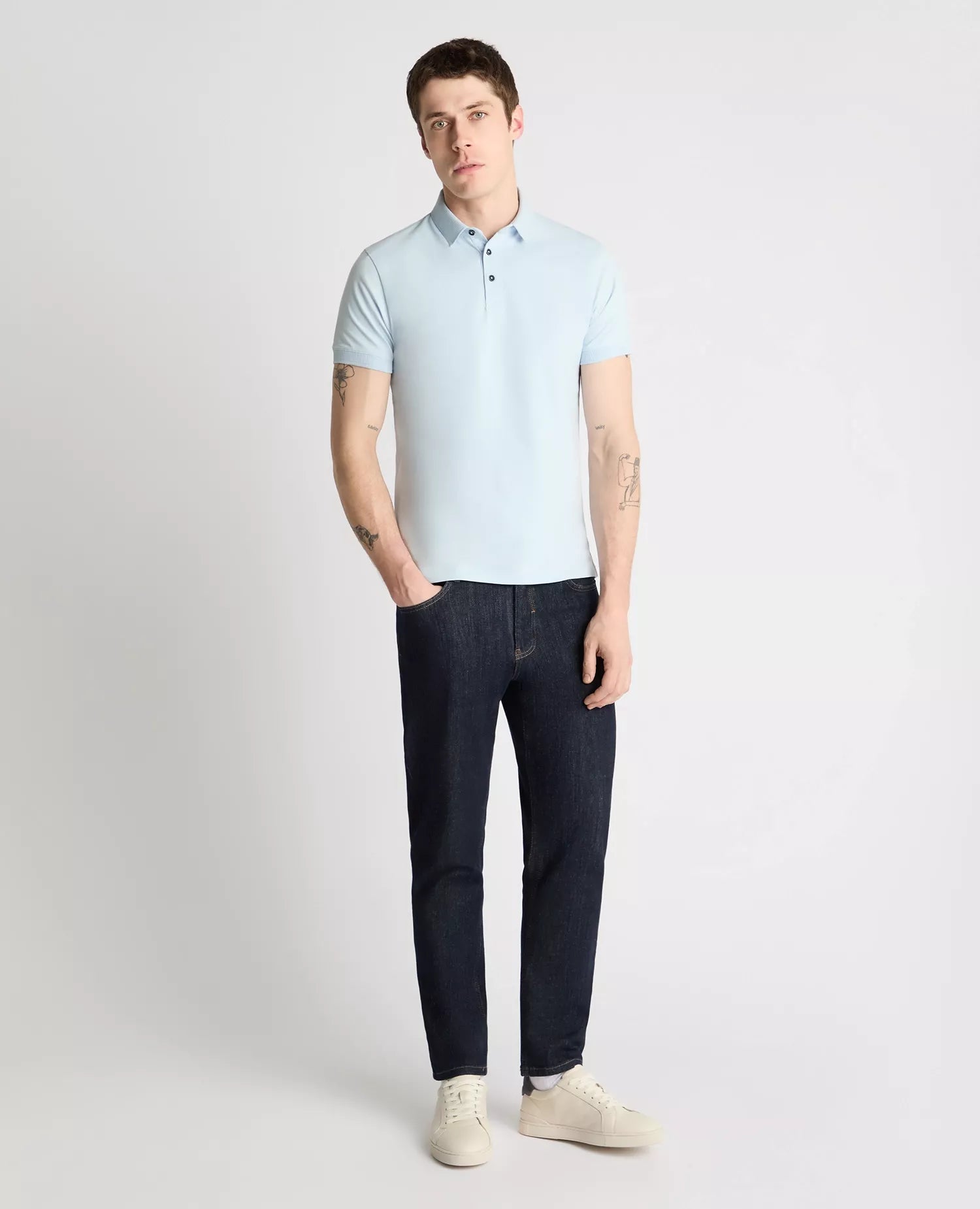 Man wearing a light blue polo shirt and dark jeans on a white background