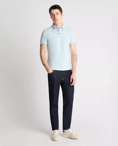 Man wearing a light blue polo shirt and dark jeans on a white background