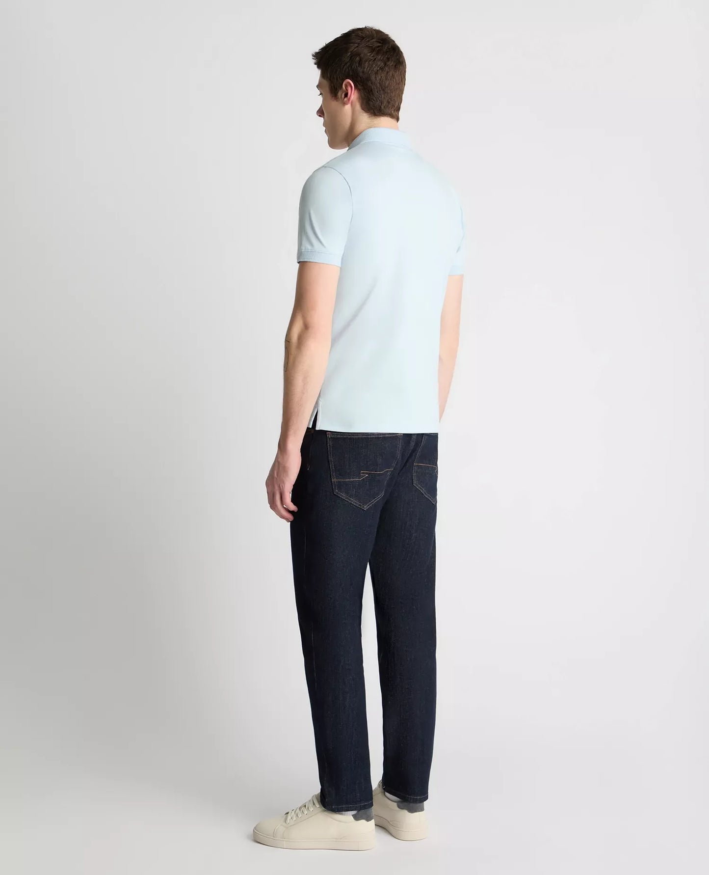 Man wearing a light blue polo shirt and dark jeans on a white background