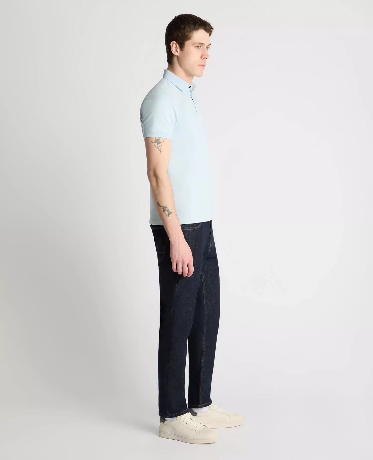 Man wearing a light blue polo shirt and dark pants on a white background