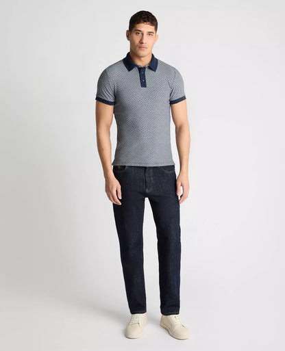 Man wearing a patterned polo shirt and dark jeans on a white background