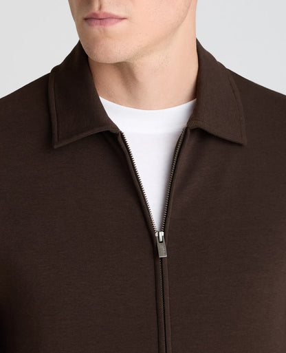 Close-up of a man wearing a dark brown zip-up collar jacket over a white crew-neck t-shirt, against a light gray background.