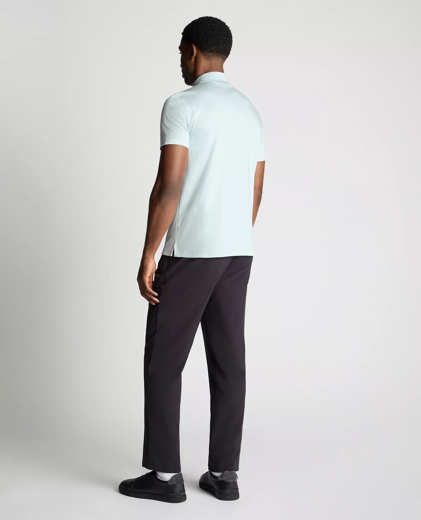 Man wearing a light blue polo shirt and black pants on a white background