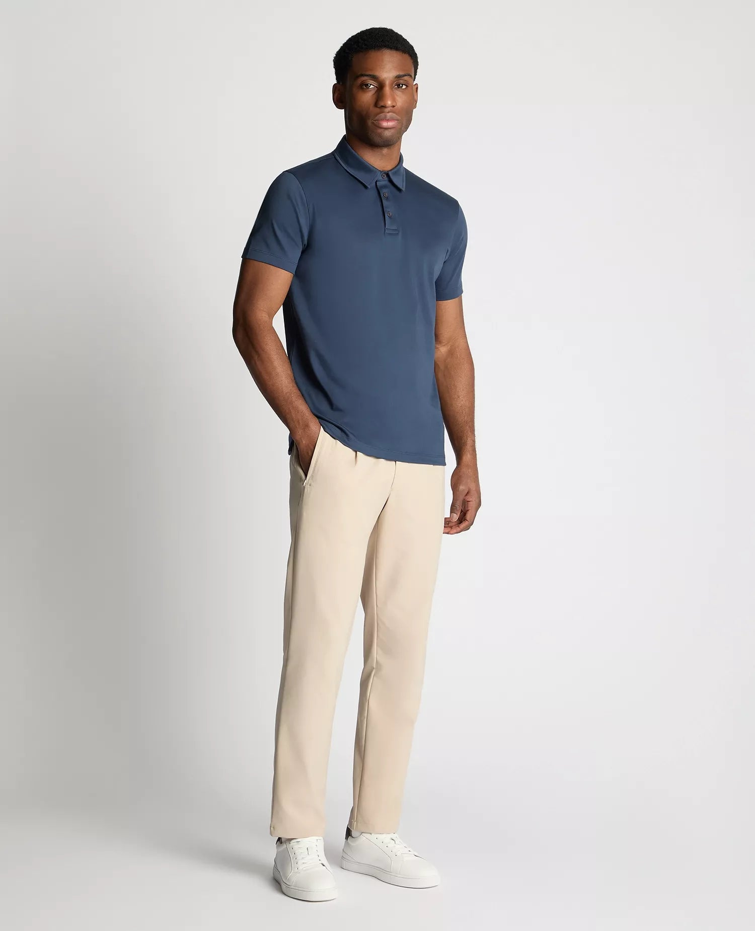 Man wearing a blue polo shirt and beige pants on a white background