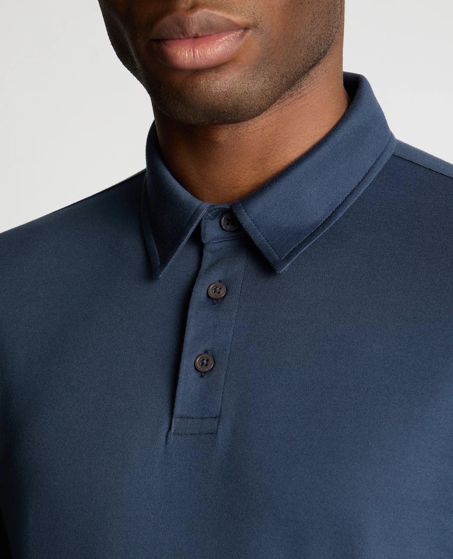 Close-up of a person wearing a blue polo shirt with a plain background